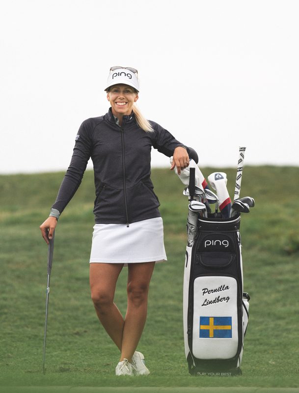 Pernilla Lindberg leans on her PING tour bag, with her name and the Swedish flag on it